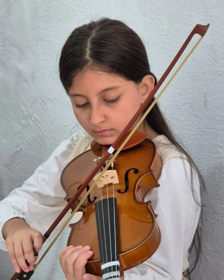 Aluna de blusa branca concentrada tocando violino