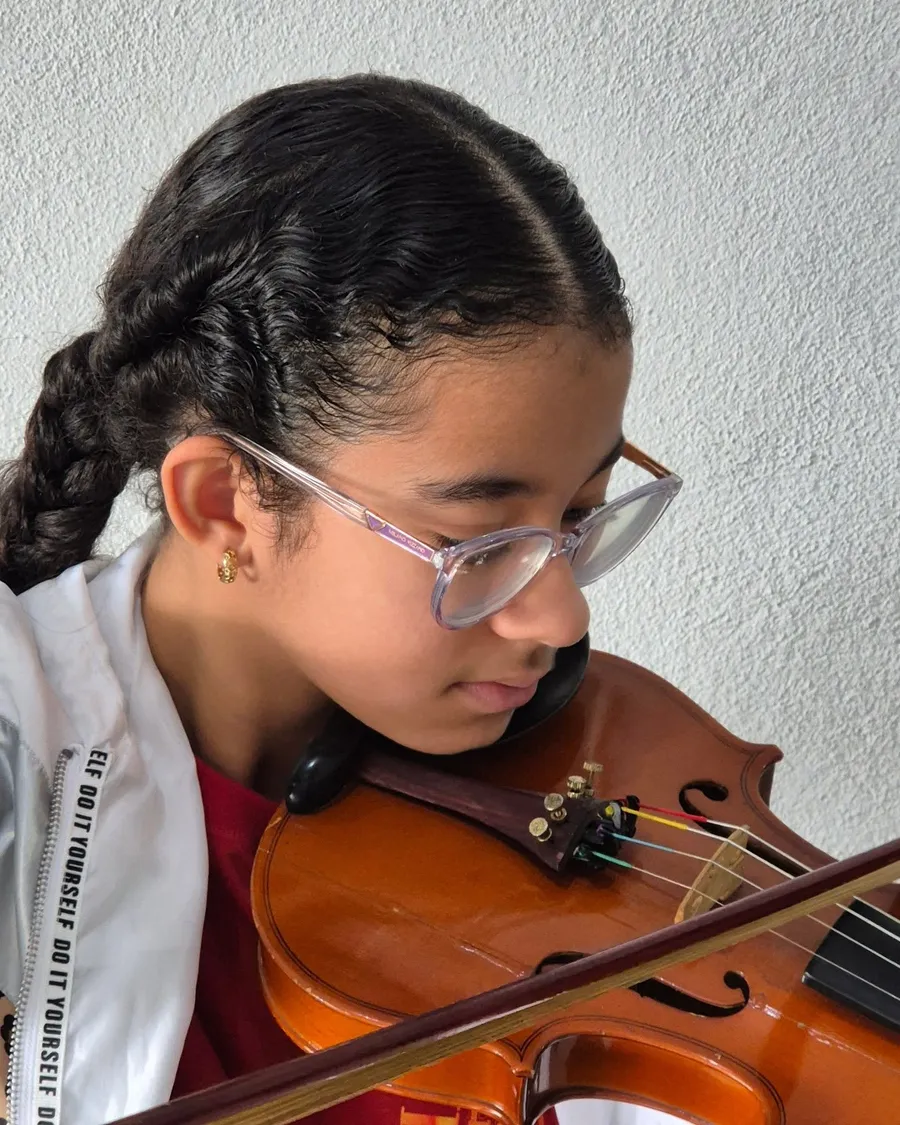 Aluna de óculos tocando violino com expressão concentrada