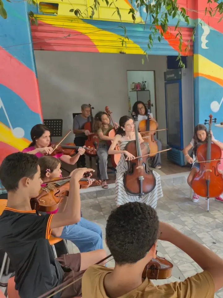 Turma de violinos e violoncelos ensaiando em roda no pátio colorido do Instituto