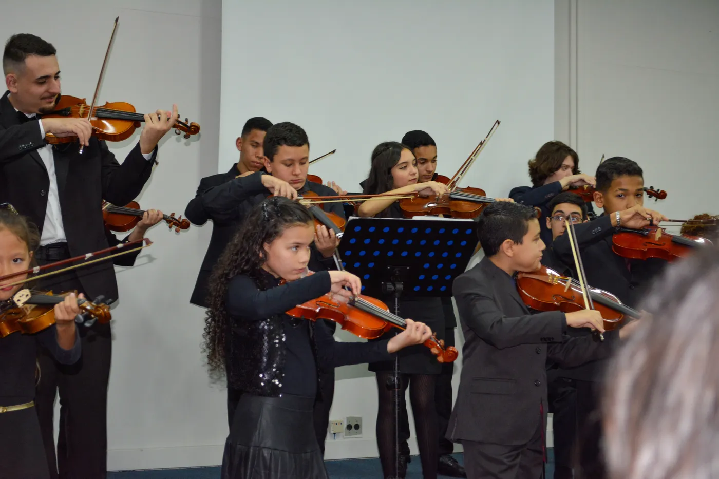 Alunos de diferentes idades tocando violino em apresentação