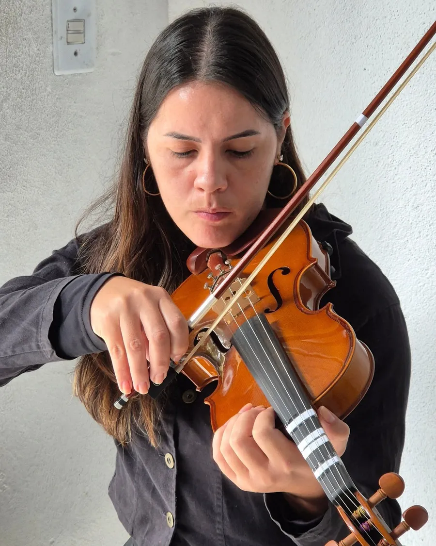 Professora tocando violino com cabelo preso e olhos fechados